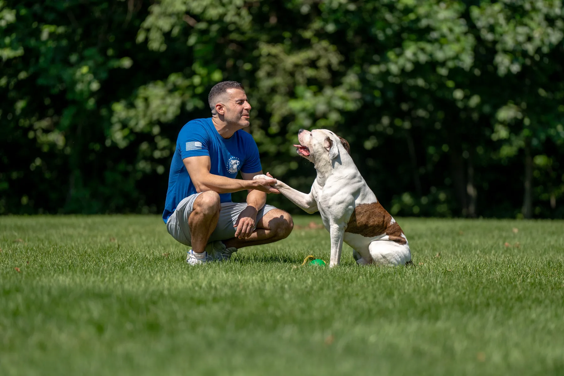 Steve Del Savio crouched on the lawn at the ranch, a white dog with a brown patch giving him a paw.