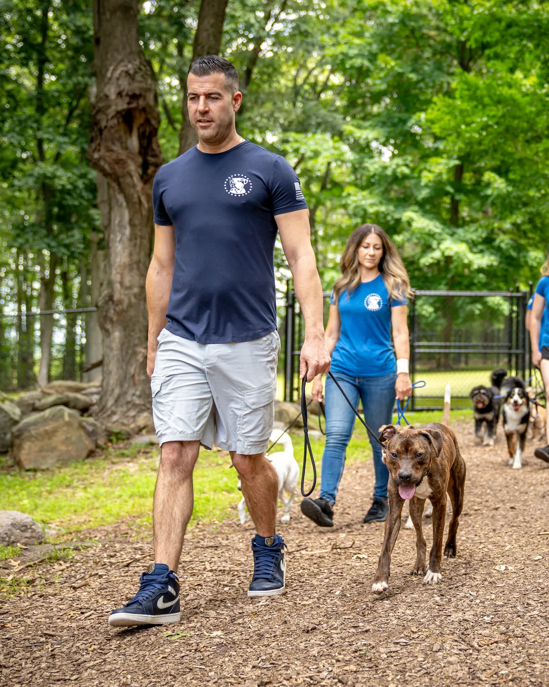 Steve Del Savio walking a dog on a loose leash along a wooded path, the team and the pack following behind.