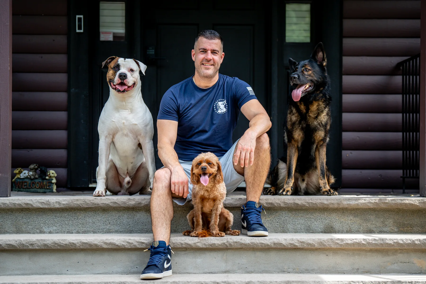 Steve Del Savio sitting on the front steps of the lodge with three dogs beside him, looking at the camera.