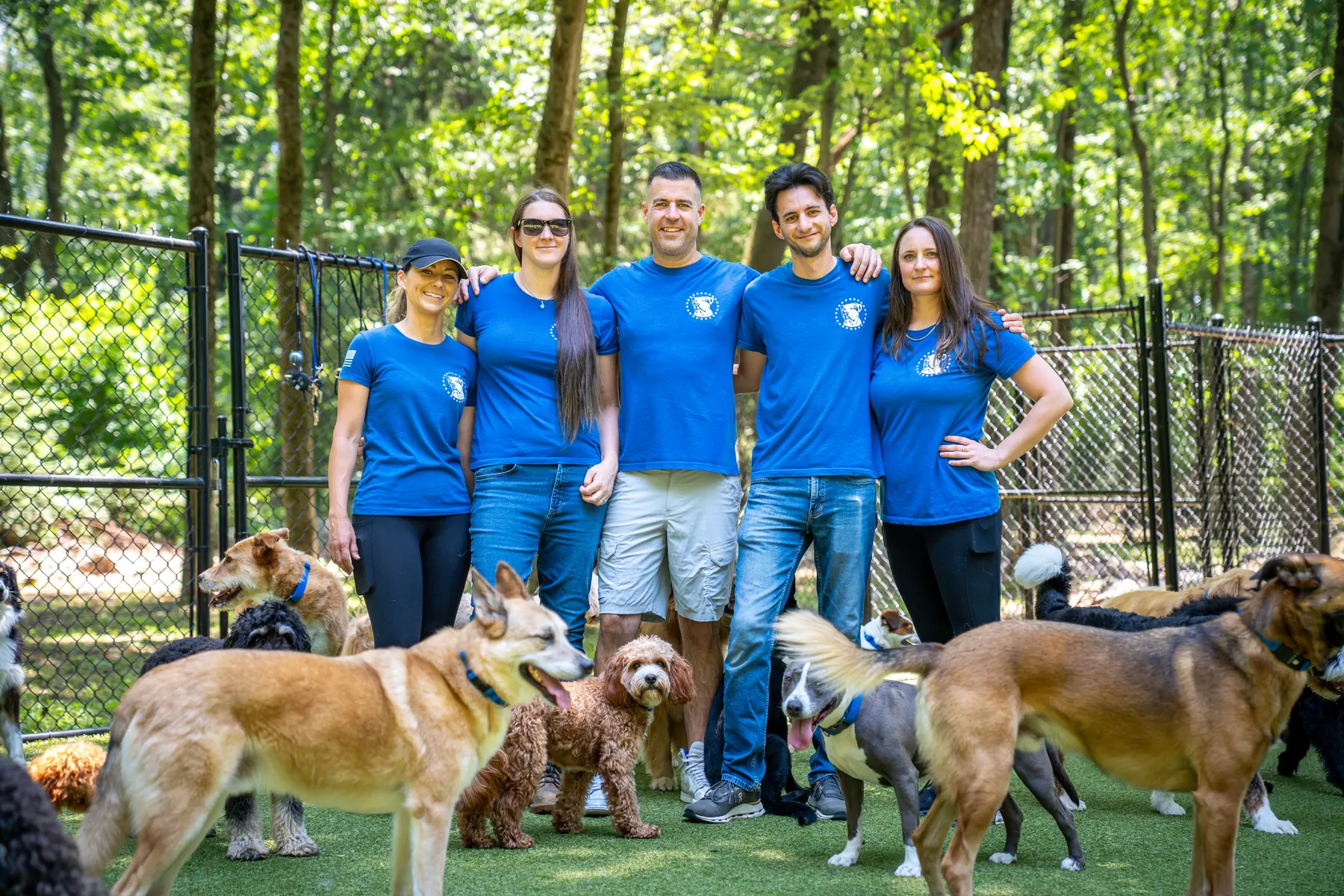 Steve Del Savio standing arm in arm with four of the team in the yard at the ranch, the pack of dogs around them.