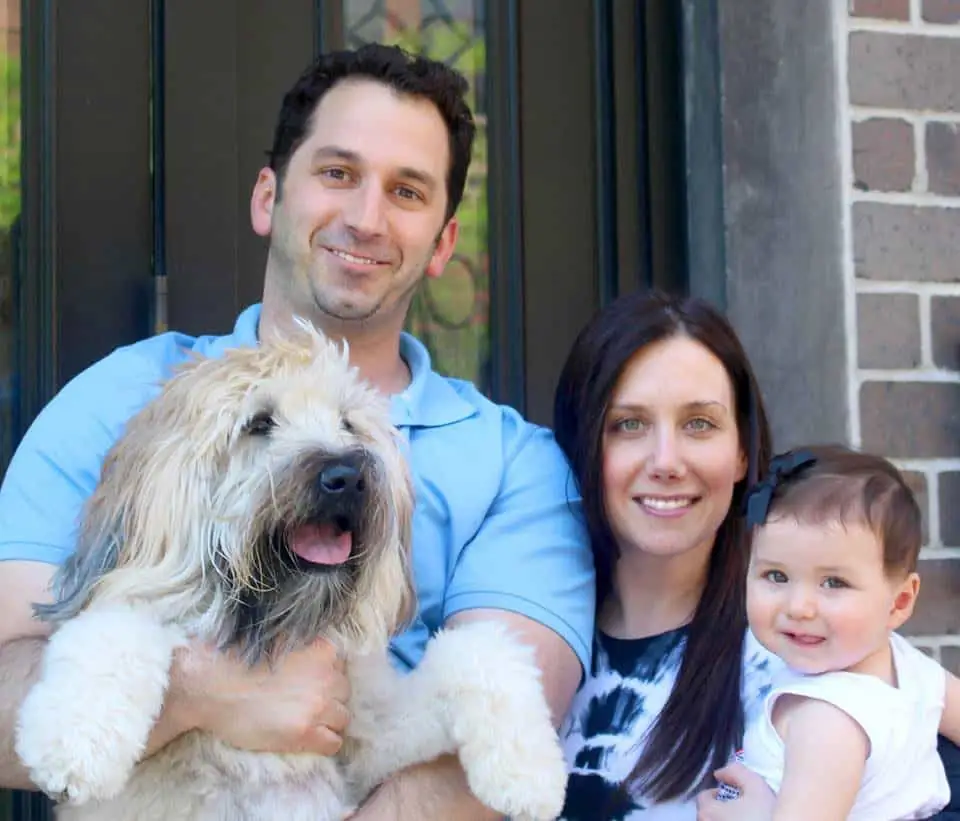 Brooke, Brian and their baby daughter at their front door, Emmitt the wheaten terrier happy in Brian's arms.
