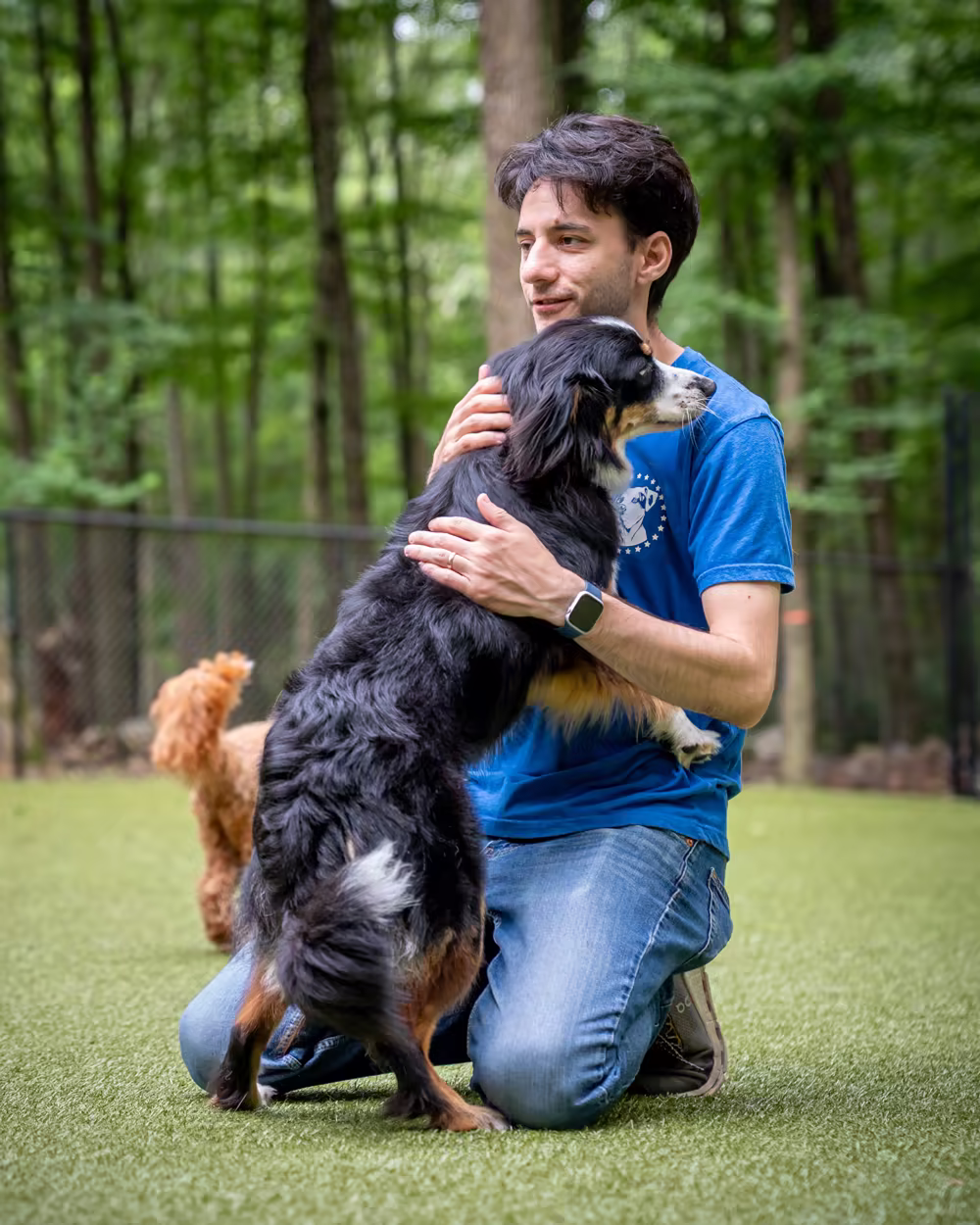 Dave DeSantis kneeling on the turf with his arms around a Bernese mountain dog