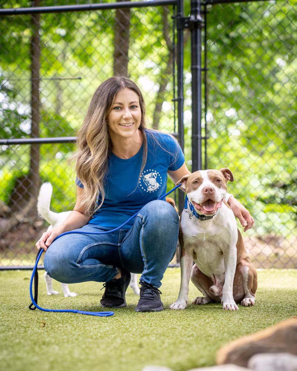 Jamie Stauhs kneeling beside a white and tan dog on the turf yard