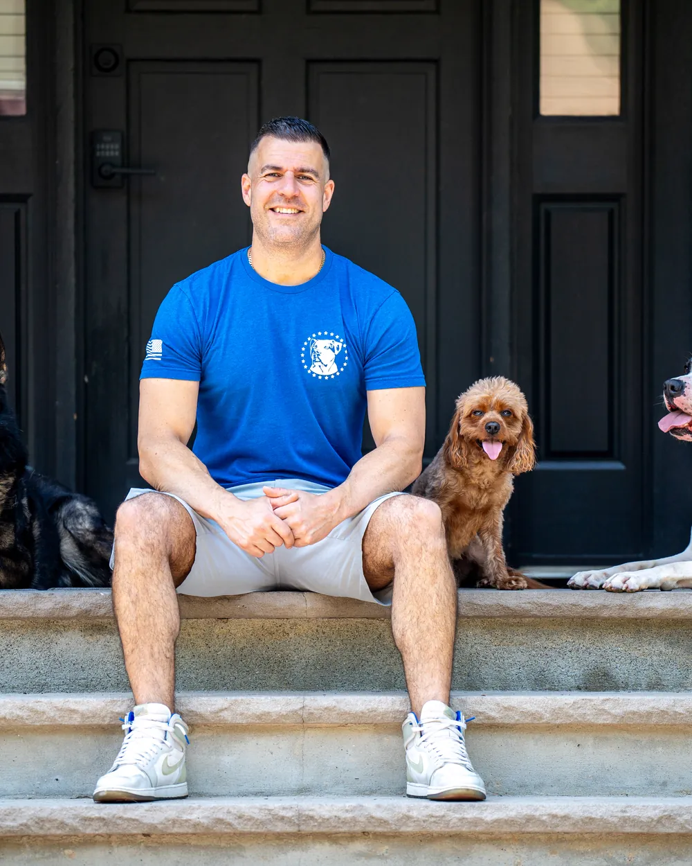 Steve Del Savio seated on the lodge steps with a shepherd, a cavapoo and a bulldog.