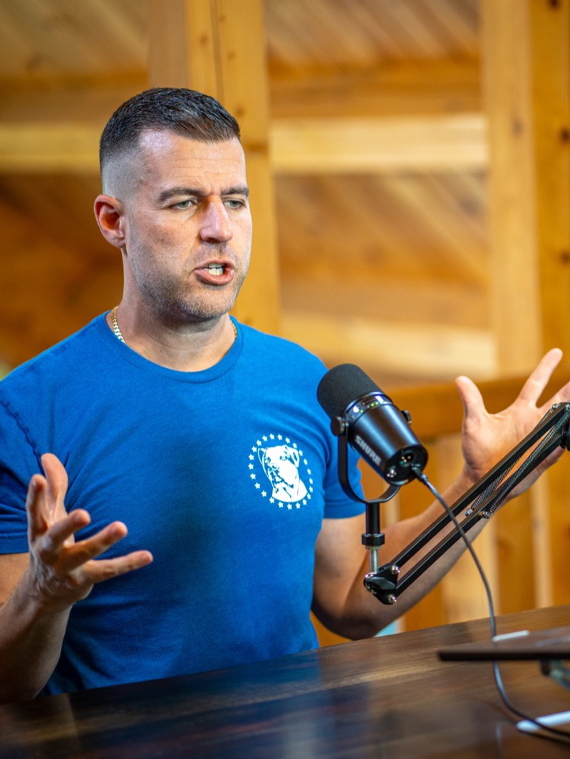 Steve Del Savio speaking to a laptop at a desk in the lodge loft, microphone in front of him.